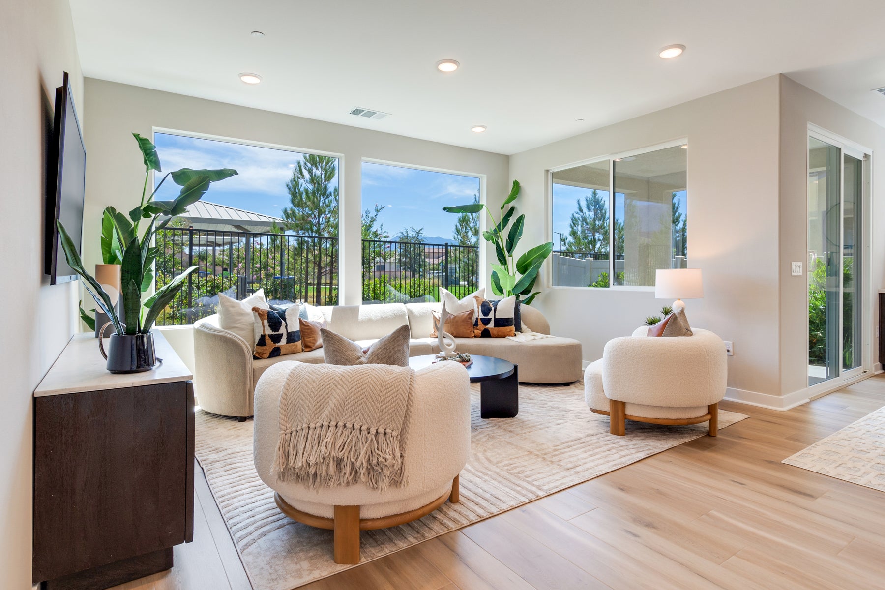Modern living room with white furniture, plants, and large windows.