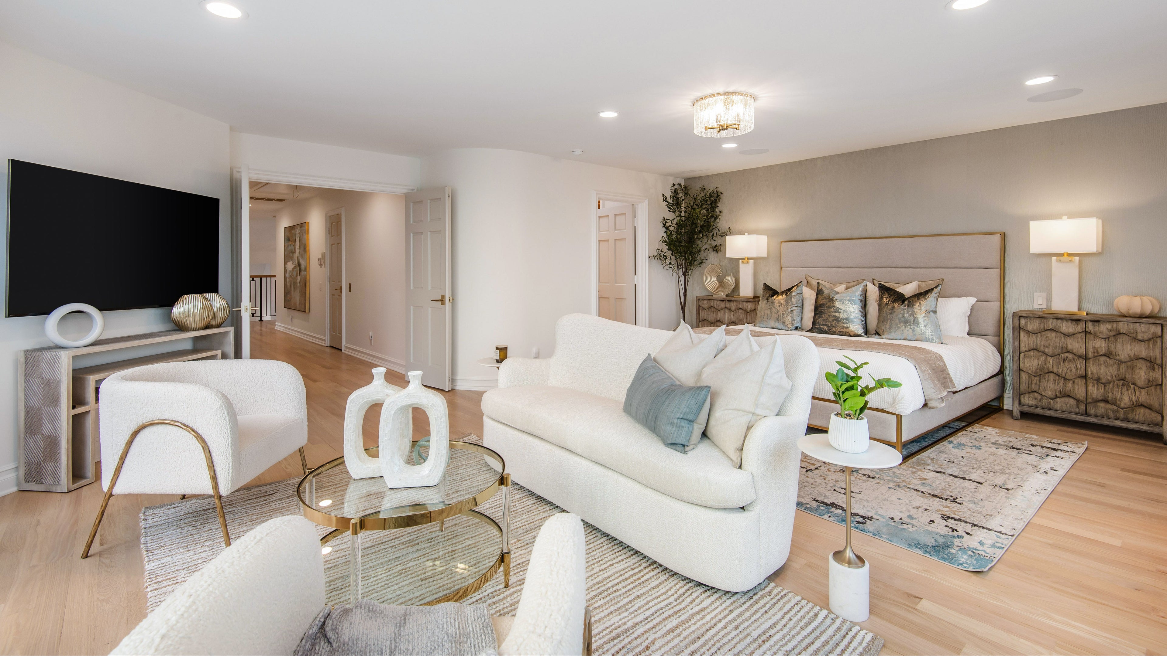 A modern bedroom with a fabric headboard, white sofa and chair sitting area and modern decor