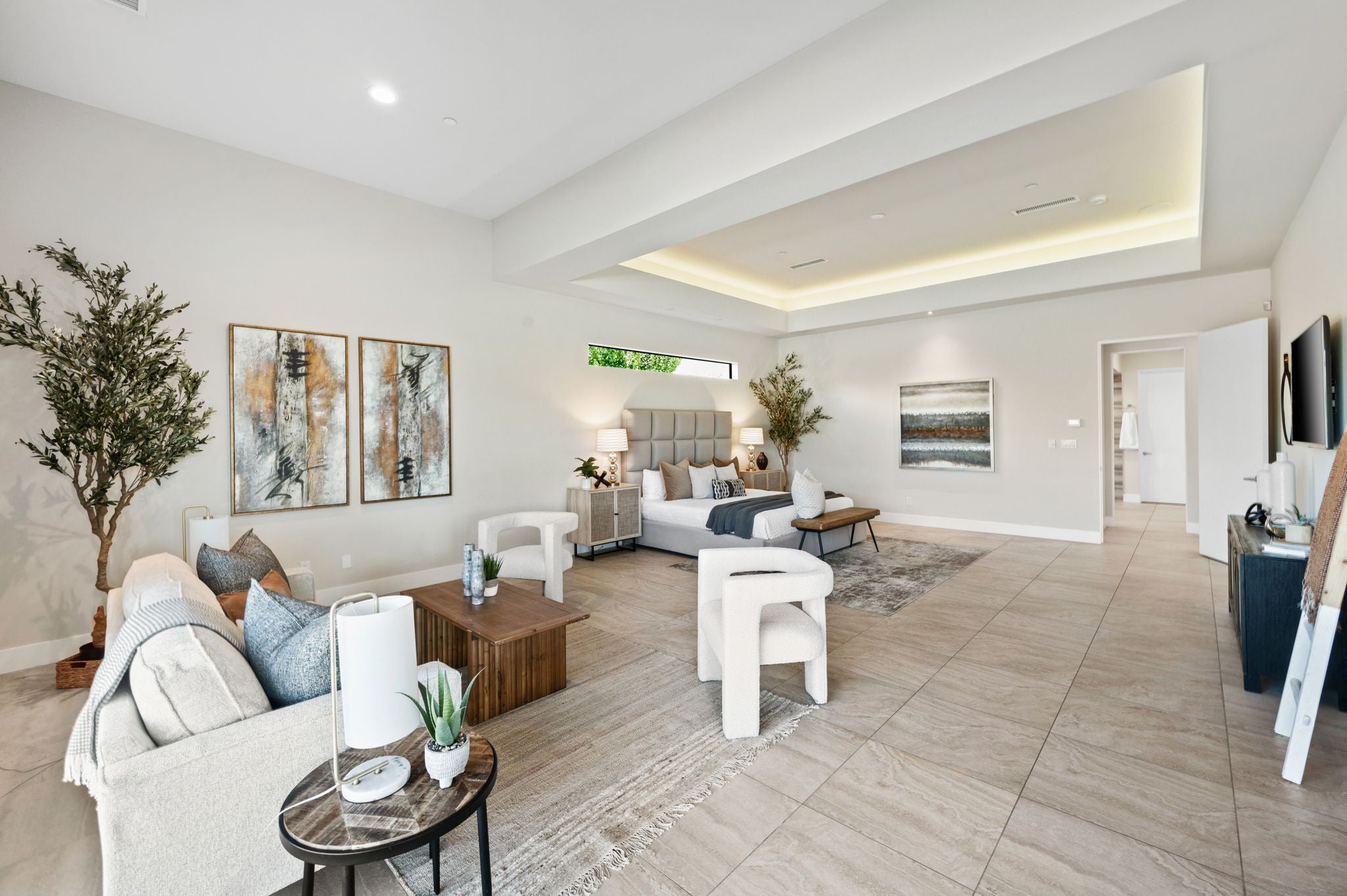 A bright, modern open-concept living and dining area with light beige tile flooring, white walls, and contemporary furniture including a light sofa, wooden coffee table, white chairs, and wall art.