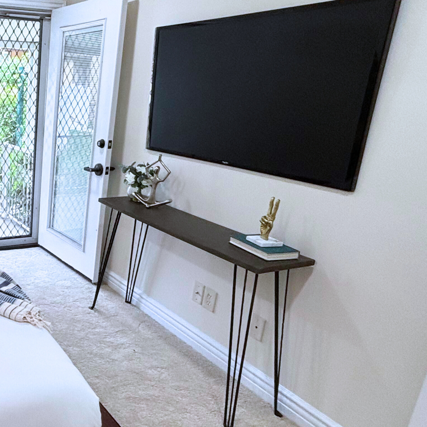 Wooden console table with metal legs against a wall with a television.