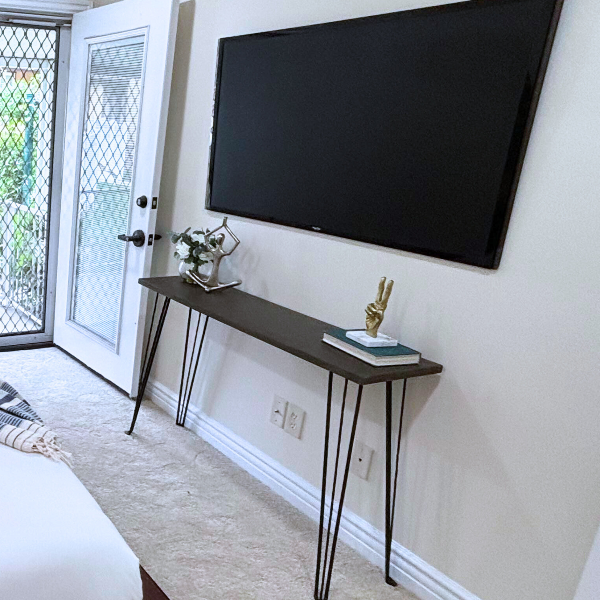 Wooden console table with metal legs against a wall with a television.