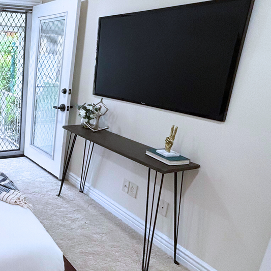 Wooden console table with metal legs against a wall with a television.
