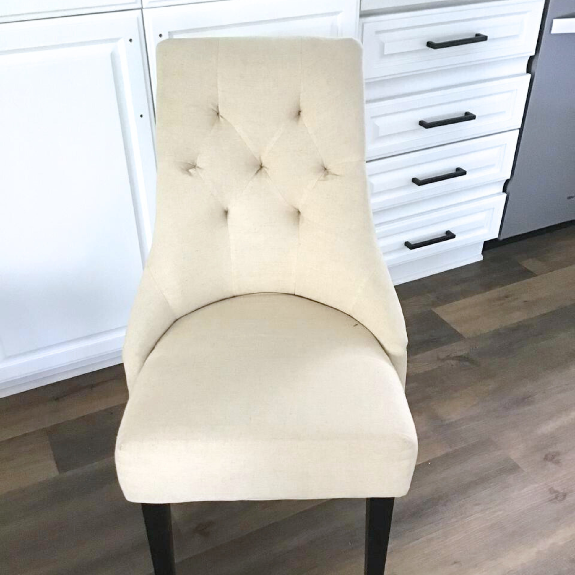 Beige upholstered chair in a room with white cabinets and wooden flooring.
