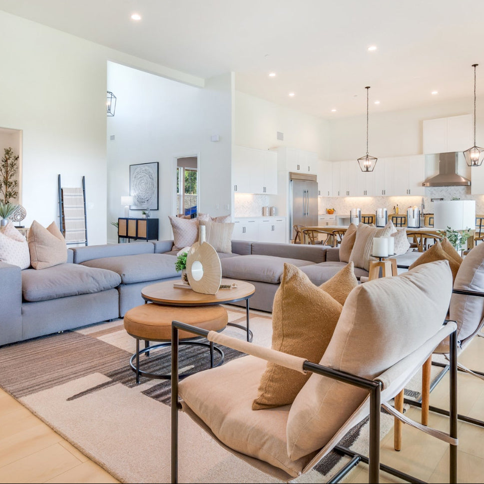 Modern living room with gray sofa, beige chairs, and kitchen in the background.