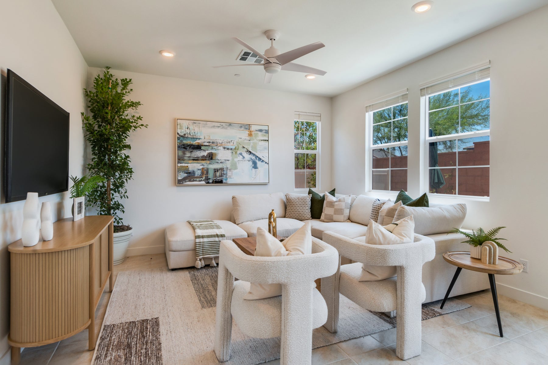 Modern living room with white furniture, decorative plants, and a painting.